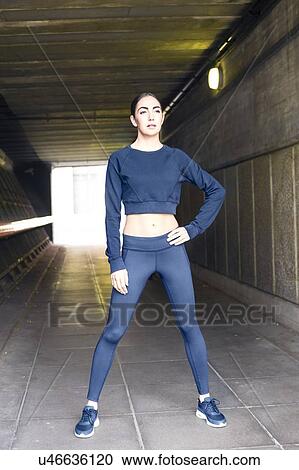 Stock Image - Young woman standing in underpass with hand on hip.. Fotosearch