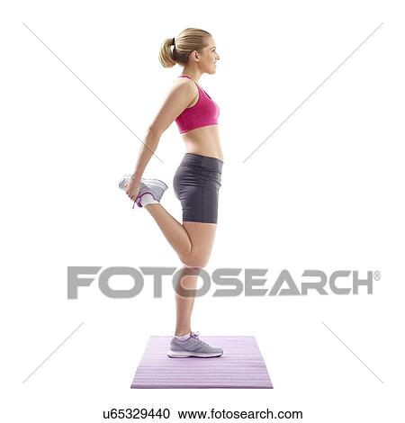 Stock Image - Young woman stretching quad muscles, studio shot.. Fotosearch