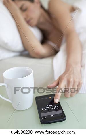 Young woman switching off alarm on smartphone View Large Photo Image Stock Image - Young woman switching off alarm on smartphone. Fotosearch