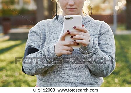 Stock Image - Young woman training in park looking at smartphone, cropped. Fotosearch