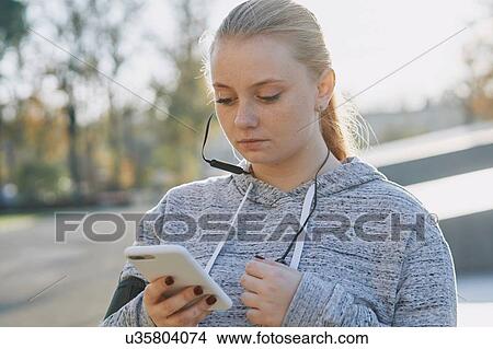 Picture - Young woman training, looking at smartphone. Fotosearch