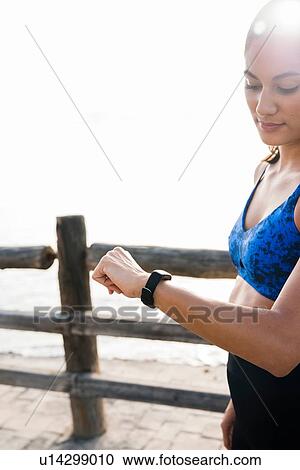 Stock Image - Young woman training on sea waterfront, looking at smartwatch. Fotosearch