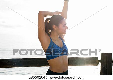 Stock Photography - Young woman training on sea waterfront, stretching arms. Fotosearch