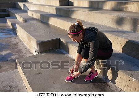 Stock Image - Young woman tying shoelace on training shoe, stretching legs. Fotosearch