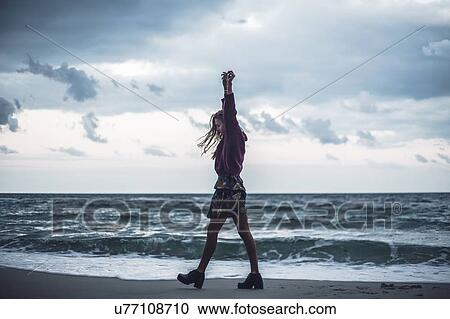 Young woman walking on beach with arms raised at dusk, Odessa Oblast, Ukraine View Large Photo Image Stock Image - Young woman walking on beach with arms raised at dusk, Odessa Oblast, Ukraine. Fotosearch