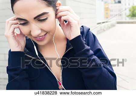 Stock Photo - Young woman wearing earphones, smiling.. Fotosearch