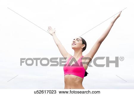 Stock Image - Young woman wearing sports bra with arms up.. Fotosearch