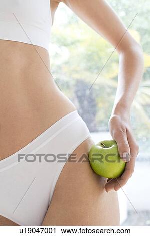 Stock Image - Young woman wearing white underwear holding apple, close up.. Fotosearch
