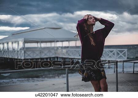 Young woman with hands in long hair leaning against beach pier at dusk, Odessa Oblast, Ukraine View Large Photo Image Stock Photo - Young woman with hands in long hair leaning against beach pier at dusk, Odessa Oblast, Ukraine. Fotosearch