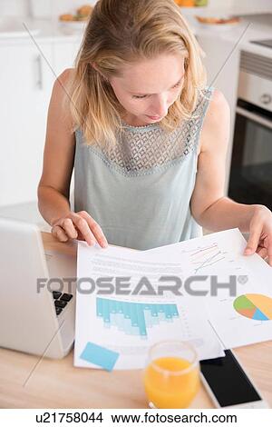 Young woman with laptop looking at paperwork at kitchen table View Large Photo Image Picture - Young woman with laptop looking at paperwork at kitchen table. Fotosearch