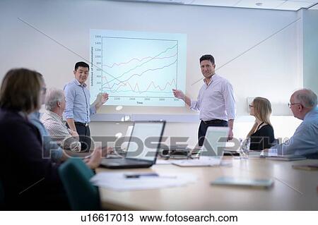 Stock Image - Younger and older scientists discussing pharmaceutical science project in meeting room. Fotosearch