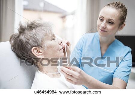 Picture - Care worker inserting nasal cannula in senior woman.. Fotosearch