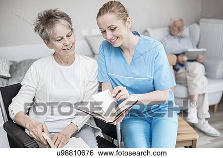 Stock Photograph - Care worker reading book with senior woman in care home.. Fotosearch