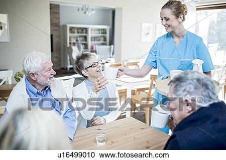 Stock Image - Care worker serving tea to senior woman in care home.. Fotosearch