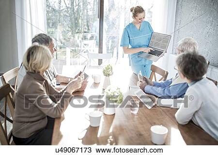 Stock Image - Care worker showing senior adults laptop in care home.. Fotosearch