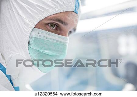 Close-up of a lab technician wearing a protective suit and face mask in a laboratory that must maintain a sterile environment. View Large Photo Image Picture - Close-up of a lab technician wearing a protective suit and face mask in a laboratory that must maintain a sterile environment.. Fotosearch