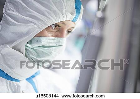 Picture - Close-up of a lab technician wearing a protective suit and face mask in a laboratory that must maintain a sterile environment.. Fotosearch