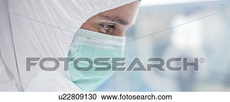 Stock Image - Close-up of a lab technician wearing a protective suit and face mask in a laboratory that must maintain a sterile environment.. Fotosearch
