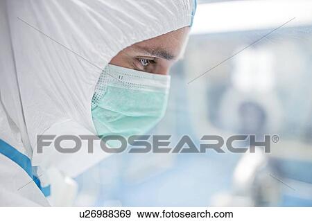 Stock Photo - Close-up of a lab technician wearing a protective suit and face mask in a laboratory that must maintain a sterile environment.. Fotosearch
