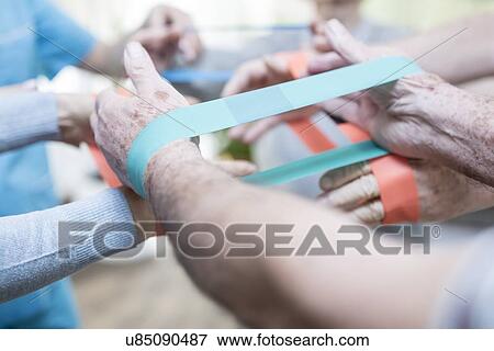 Stock Photo - Close up of senior adults using resistance bands in exercise class.. Fotosearch