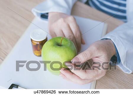 Stock Photograph - Doctor advising apple instead of pills, conceptual image.. Fotosearch