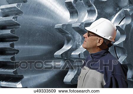 Stock Photo - Engineer examining large steel and titanium gears and cogs.. Fotosearch