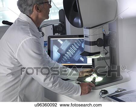 Stock Image - Engineer using a stereo microscope to inspect a manufactured component during the quality control process.. Fotosearch