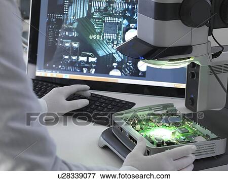 Stock Photo - Engineer using a stereo microscope to inspect a printed circuit board during the quality control process.. Fotosearch