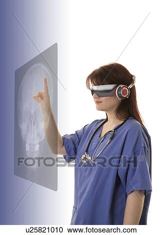 Stock Image - Female doctor wearing virtual reality headset and examining X-ray.. Fotosearch