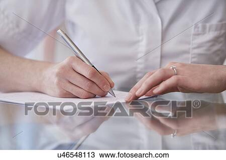 Stock Image - Female osteopath making notes, close up.. Fotosearch