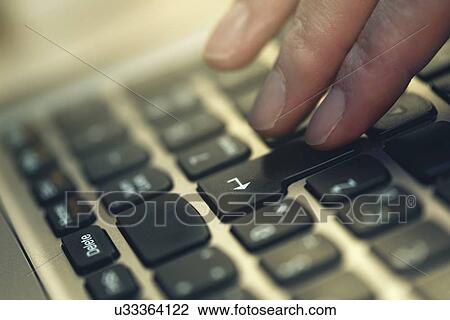 Stock Image - Finger pressing Enter key on laptop keyboard, conceptual image.. Fotosearch