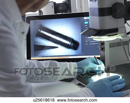 Stock Photo - Forensic scientist using a 3d stereo microscope to view markings on a bullet in the laboratory during a criminal investigation.. Fotosearch