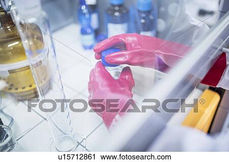 Stock Image - Lab technician using a laminar flow hood and thick gloves while working with dangerous chemicals.. Fotosearch