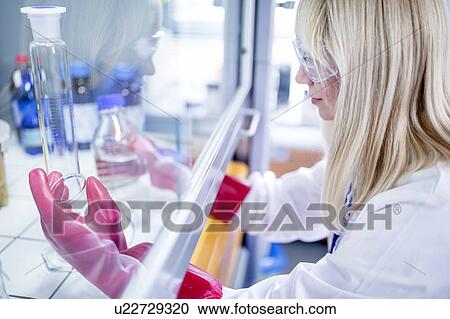 Stock Image - Lab technician using a laminar flow hood, thick gloves and safety goggles while working with dangerous chemicals.. Fotosearch