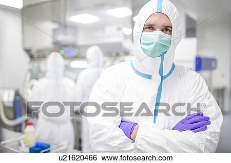 Stock Photograph - Lab technician wearing a protective suit and face mask in a laboratory that must maintain a sterile environment.. Fotosearch