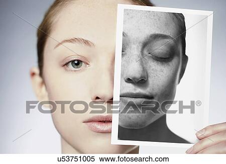 Stock Photography - MODEL RELEASED. Sun damage. Woman holding a photograph in front of her face showing the damage sun exposure has done to her skin.. Fotosearch