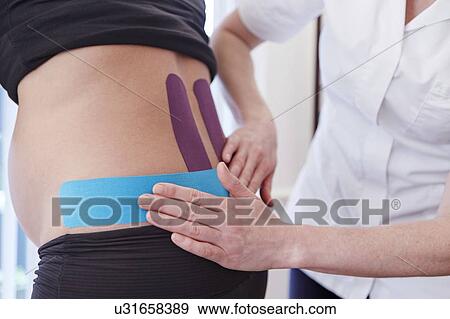 Stock Photo - Osteopath applying tape to pregnant patient.. Fotosearch