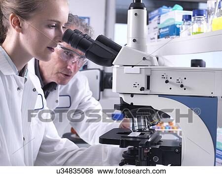 Scientists viewing a sample on a glass slide under a light microscope. View Large Photo Image Stock Photo - Scientists viewing a sample on a glass slide under a light microscope.. Fotosearch