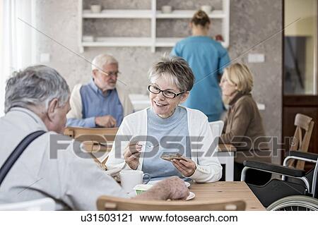 Stock Image - Senior adults eating meal in care home.. Fotosearch