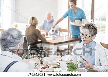 Stock Image - Senior adults eating meal in care home.. Fotosearch