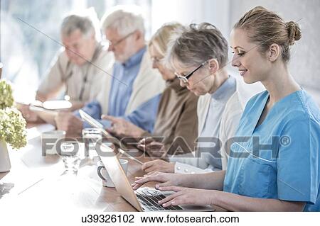 Stock Image - Senior adults in care home using digital tablets with care worker.. Fotosearch