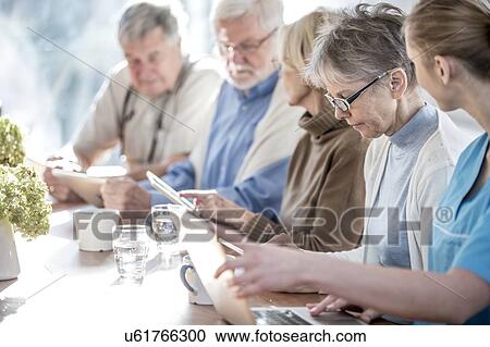 Stock Image - Senior adults in care home using digital tablets with care worker.. Fotosearch