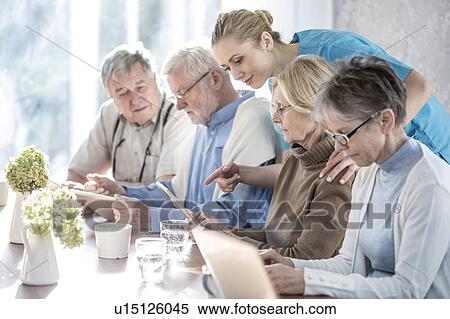 Stock Photography - Senior adults in care home using digital tablets with care worker.. Fotosearch