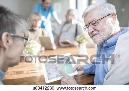 Senior adults looking at photos on digital tablet in care home. View Large Photo Image Stock Image - Senior adults looking at photos on digital tablet in care home.. Fotosearch