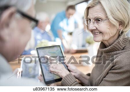 Senior adults looking at photos on digital tablet in care home. View Large Photo Image Stock Photography - Senior adults looking at photos on digital tablet in care home.. Fotosearch