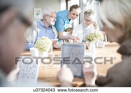 Stock Image - Senior adults playing games on digital tablets in care home.. Fotosearch