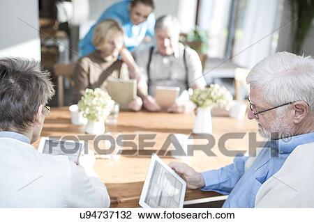 Stock Image - Senior adults using digital tablets in care home.. Fotosearch