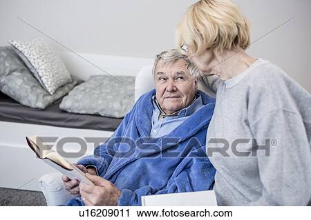 Stock Image - Senior couple reading book in care home.. Fotosearch