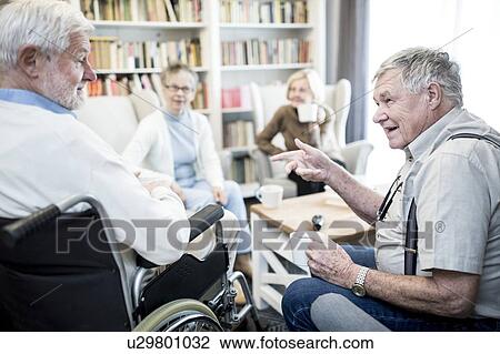 Stock Image - Senior man in wheelchair talking to fiend in care home.. Fotosearch