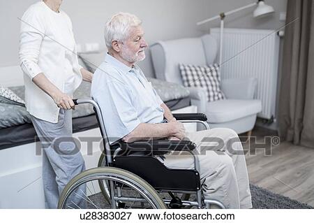 Stock Photo - Senior man in wheelchair with woman in care home.. Fotosearch